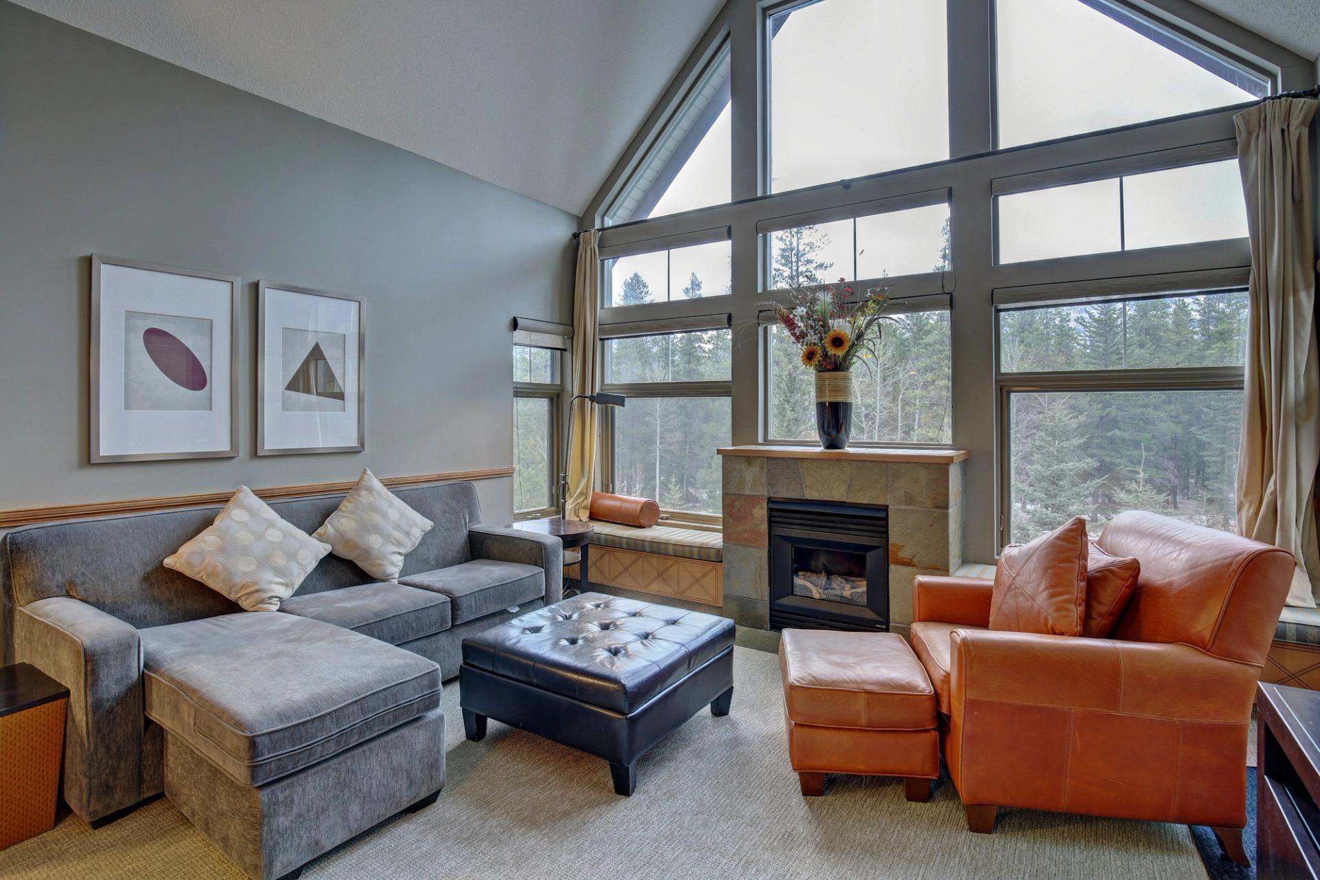 Living room with large windows, fireplace, gray sectional, and orange armchair.