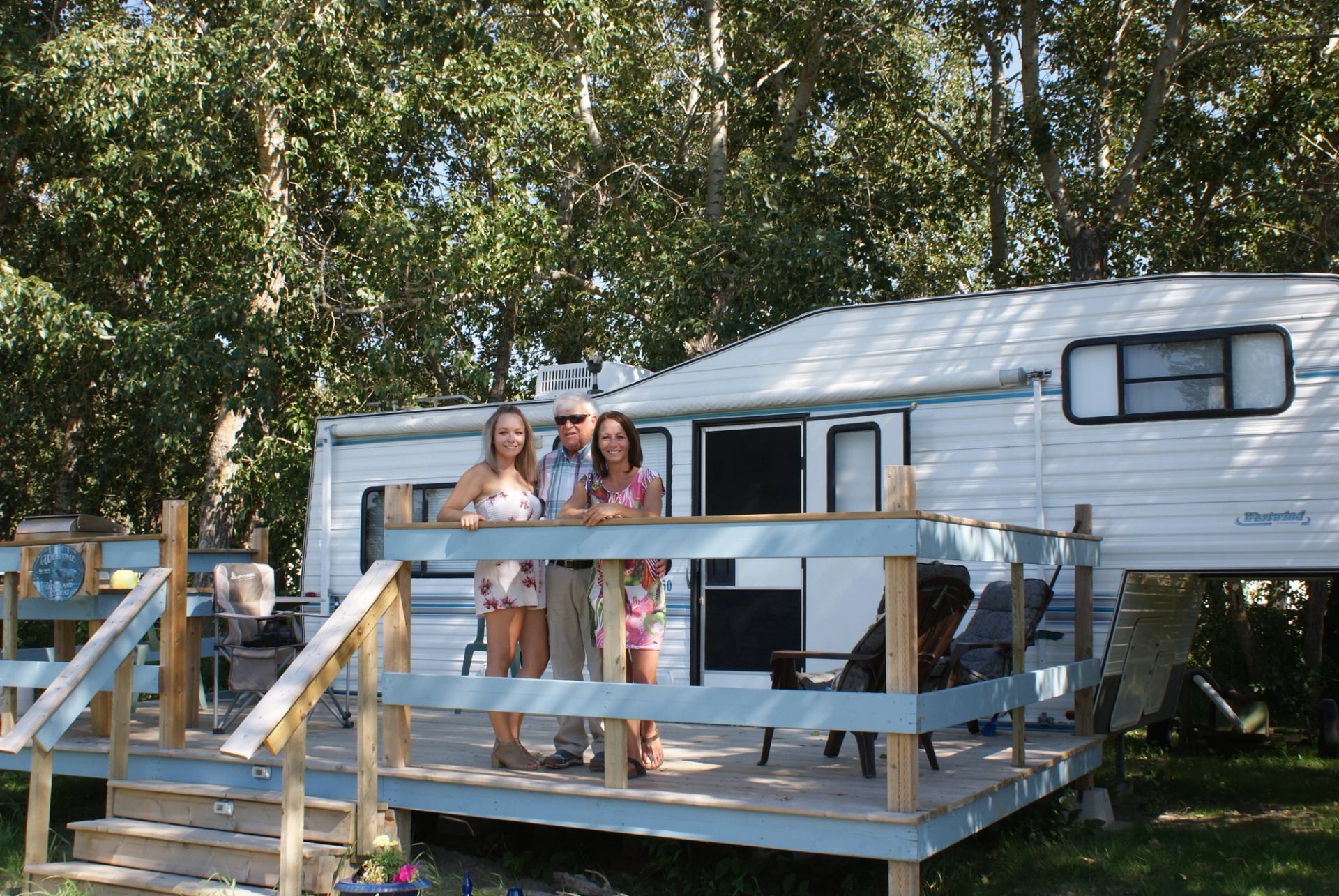 Camper trailer with deck, people, and trees at High Eagle RV Park.