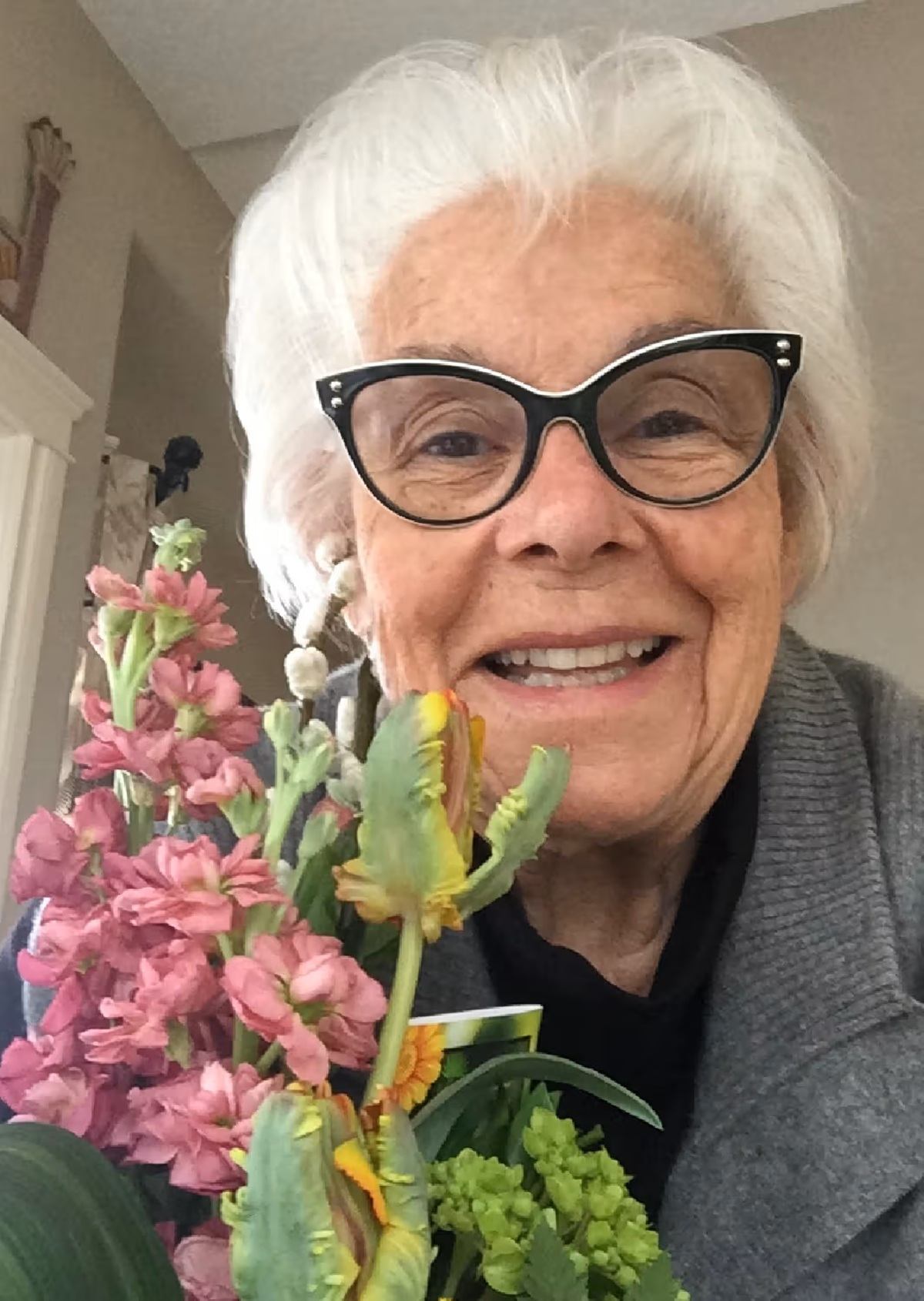 Person with white hair and black glasses holding a colourful bouquet of flowers indoors.