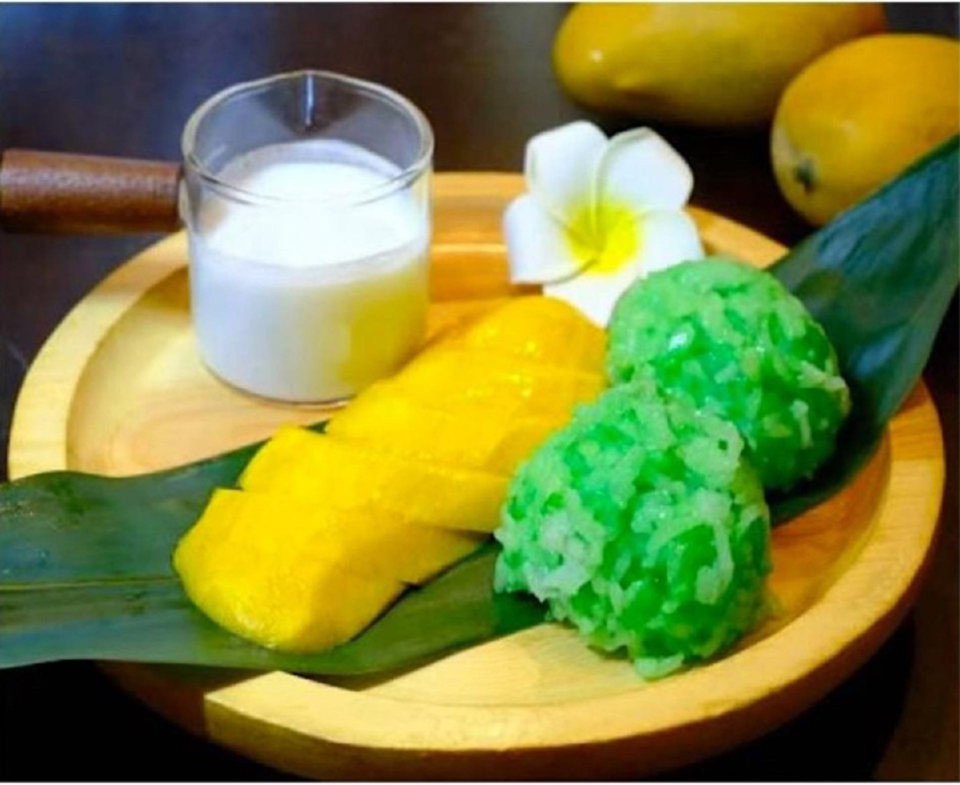 Mango sticky rice with coconut milk, mango slices, and flower on a wooden plate.