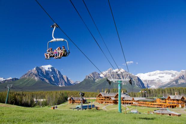 People riding a chairlift in the summer with views of the lodge building at Lake Louise in Banff National Park.