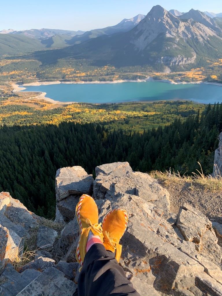 View from a rocky cliff overlooking a turquoise lake and mountain range.