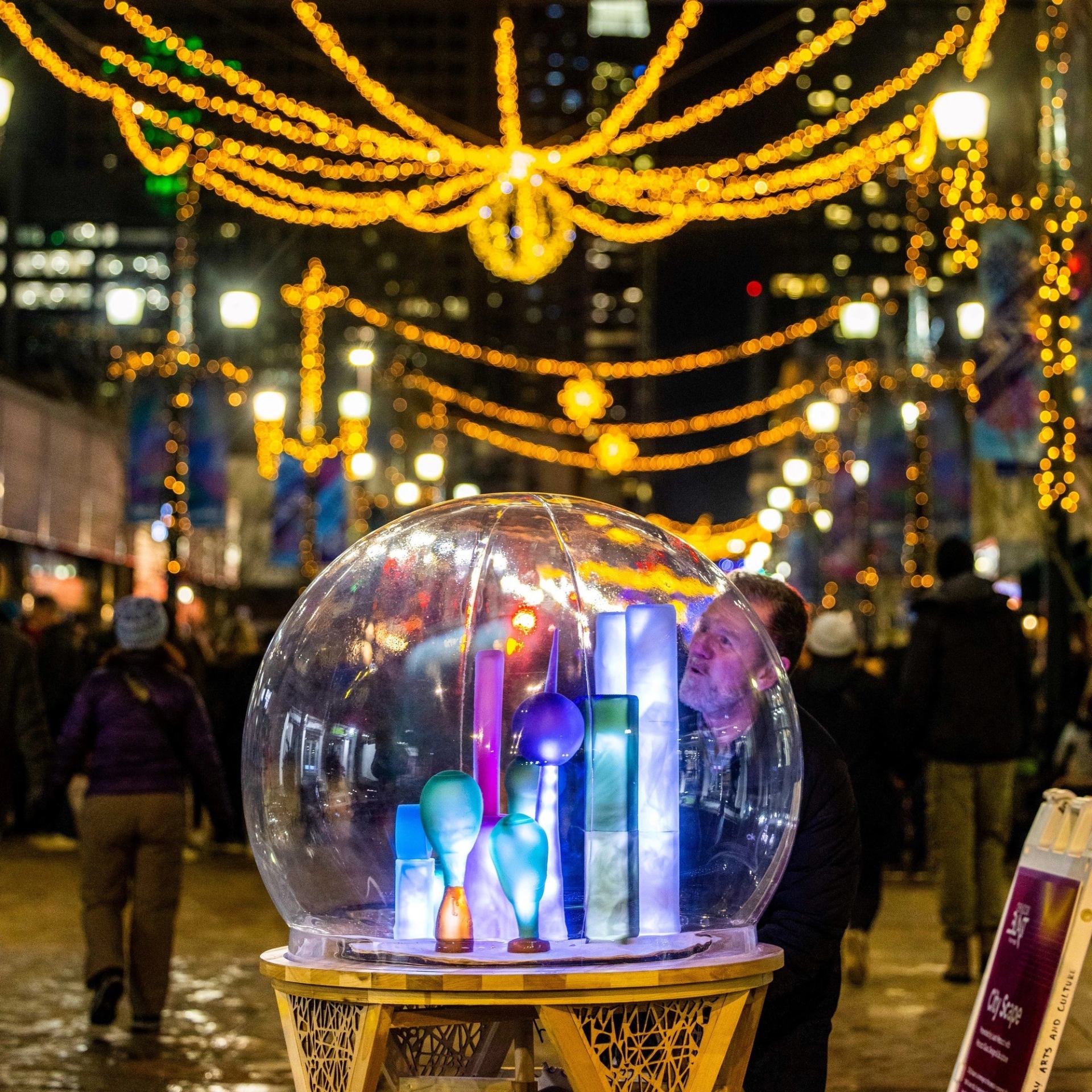 Child looks into colorful light globe on a busy street.