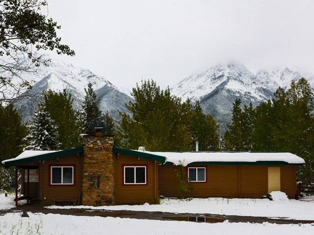 Snow-covered cabin with stone chimney and mountain backdrop.