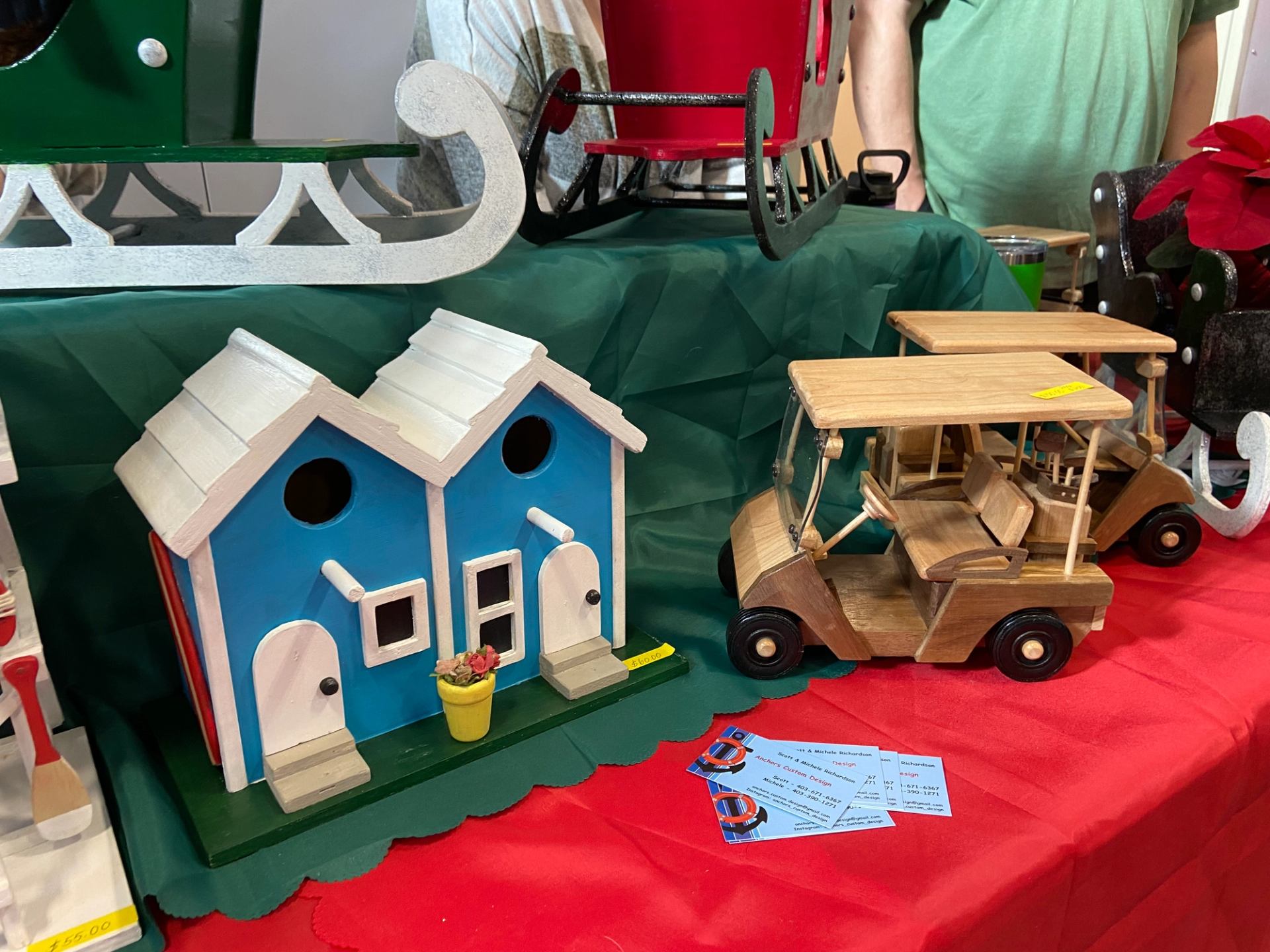 Handcrafted wooden birdhouse and toy golf cart displayed on a festive table.