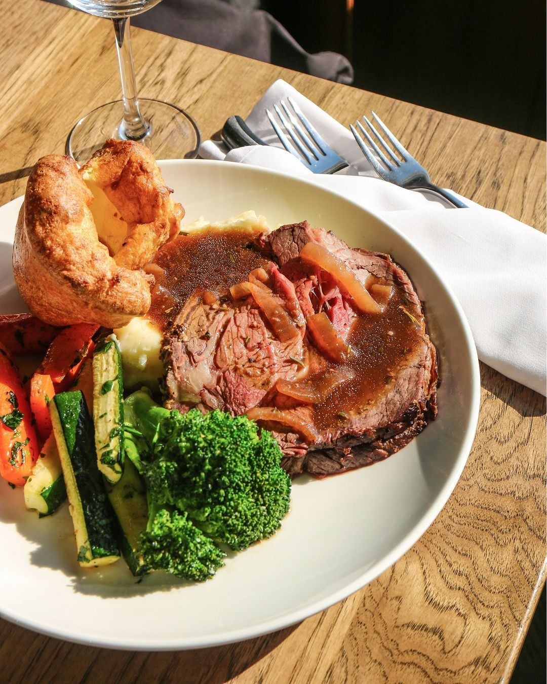Roast meat with gravy, veggies, and Yorkshire pudding on a wooden table.