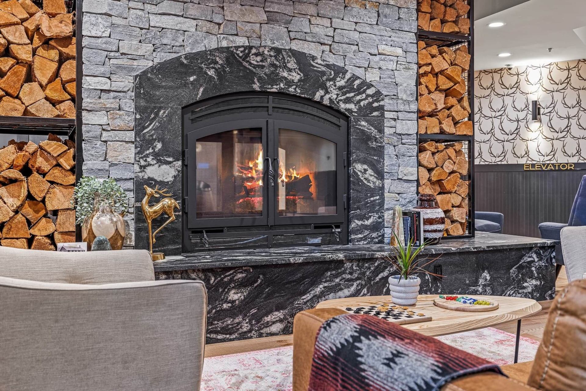 Stone fireplace with stacked firewood, cozy seating, and warm wood accents in Everwild Hotel lobby.