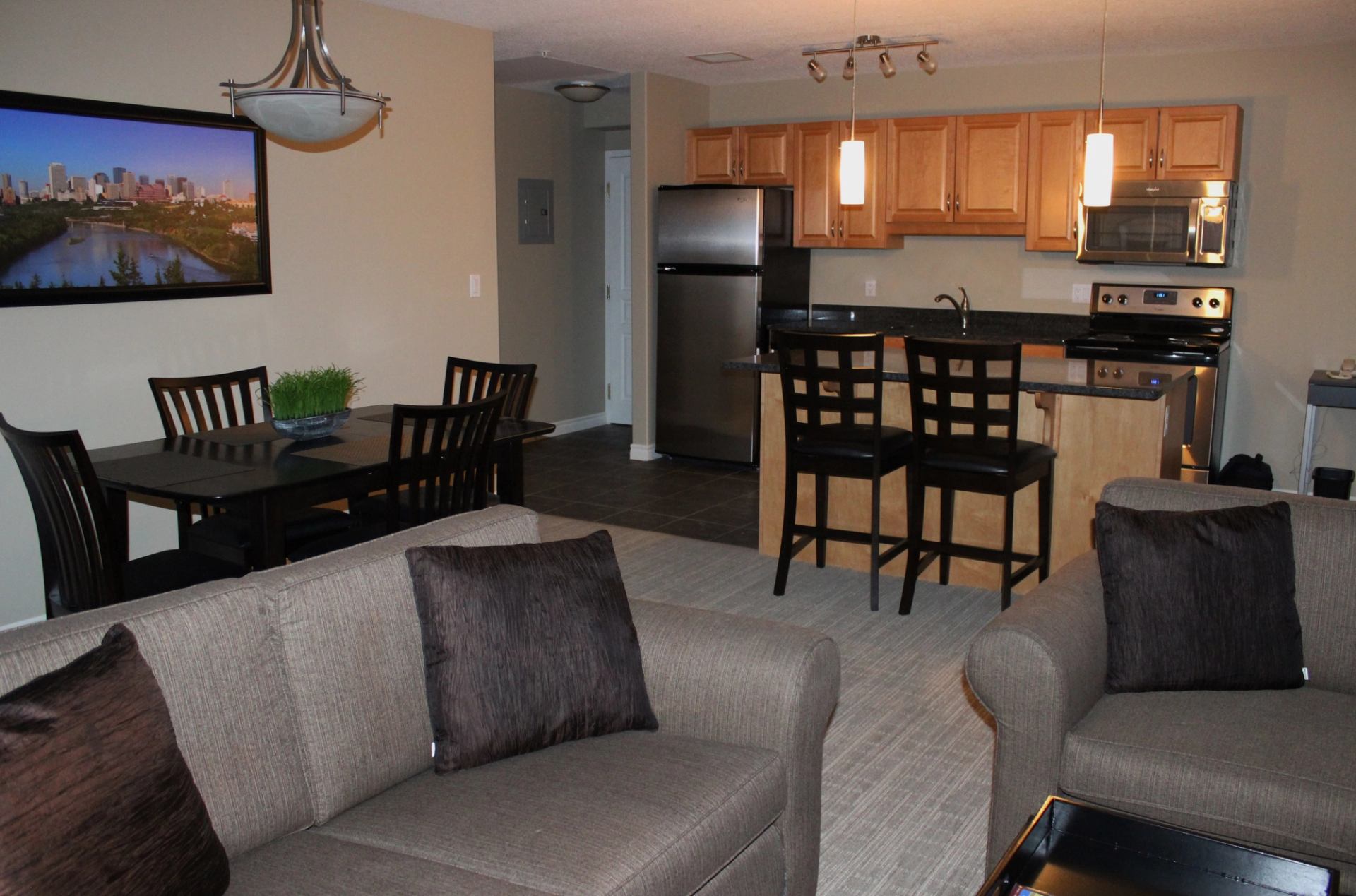 Suite with kitchen, dining table, bar stools, stainless appliances, and two cushioned sofas.