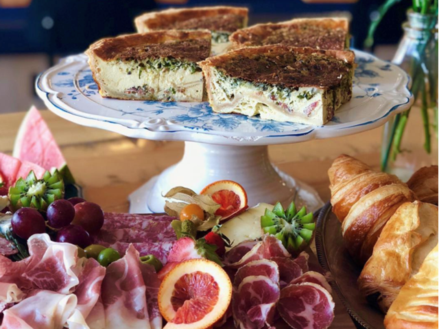 Sandwich wedges on cake stand with charcuterie, fruit slices and croissants.