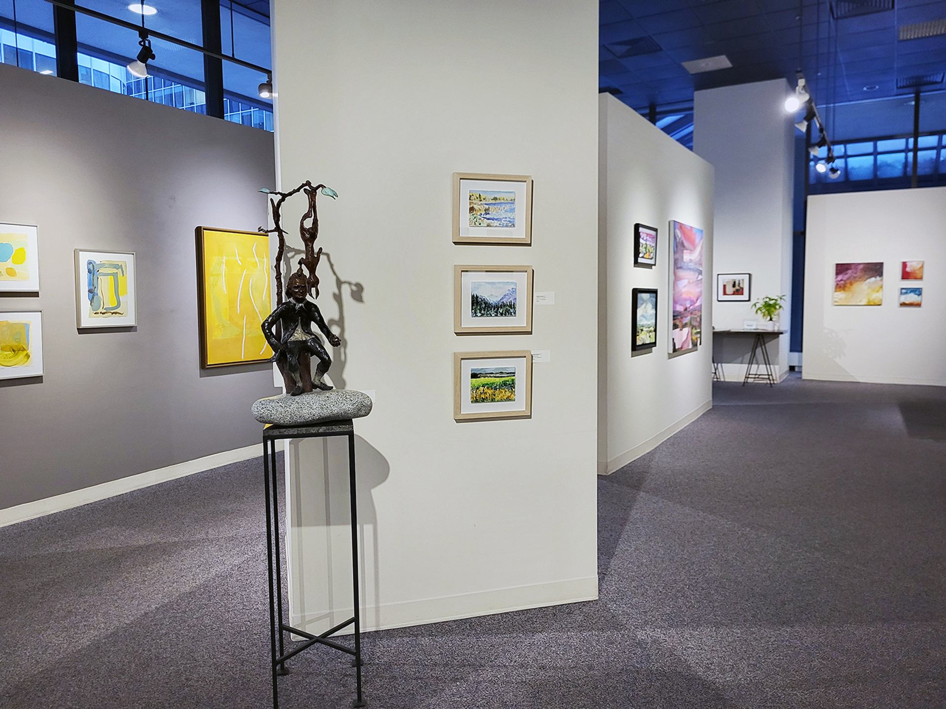Art gallery interior with colorful paintings on walls and a bronze sculpture on display.