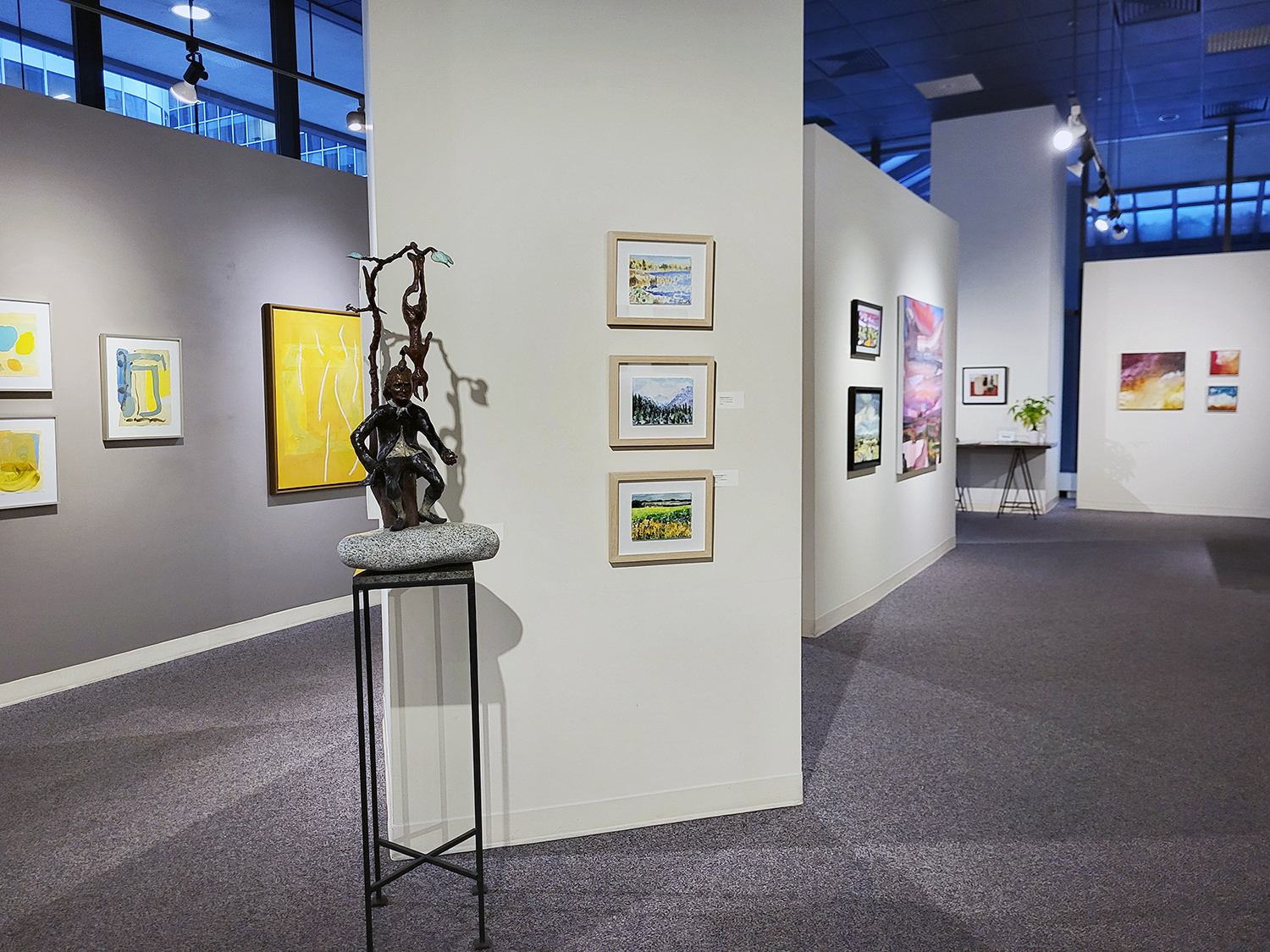 Art gallery interior with colorful paintings on walls and a bronze sculpture on display.