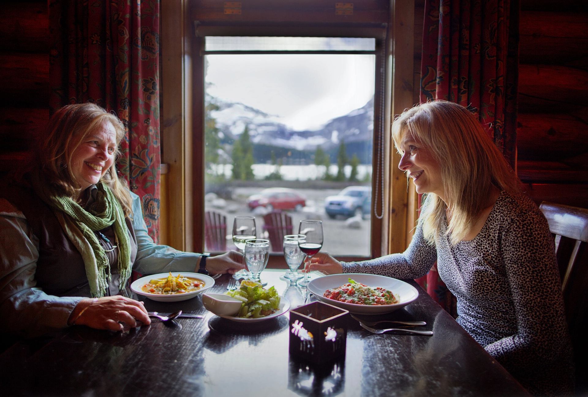 Two ladies dining at the lodge, enjoying a glass of wine and meal with a window by their table.