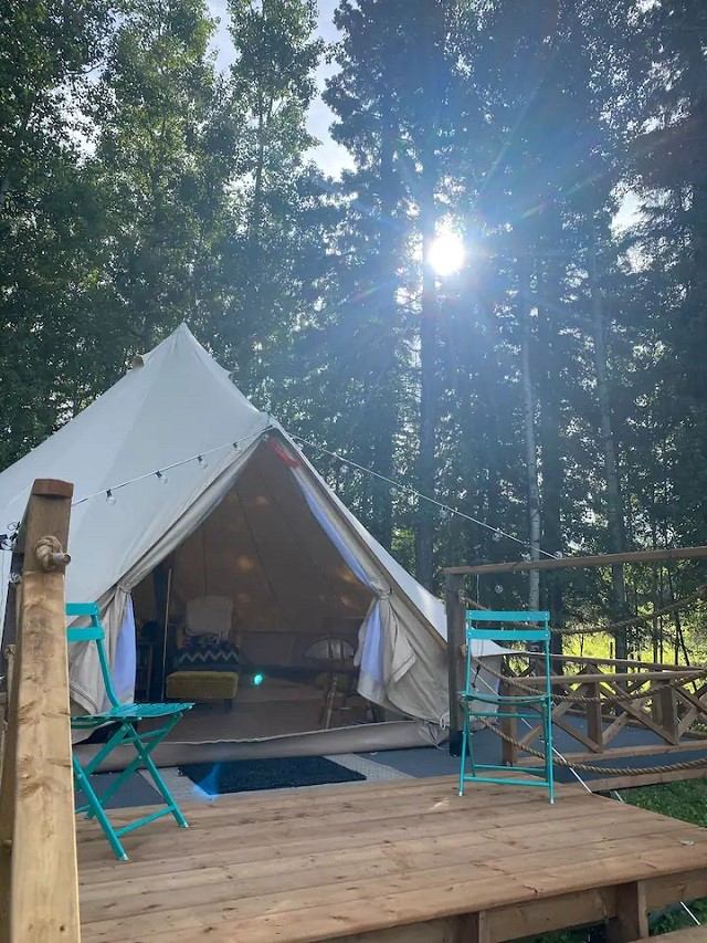 White canvas tent on wooden deck with turquoise chairs in a sunny forest
