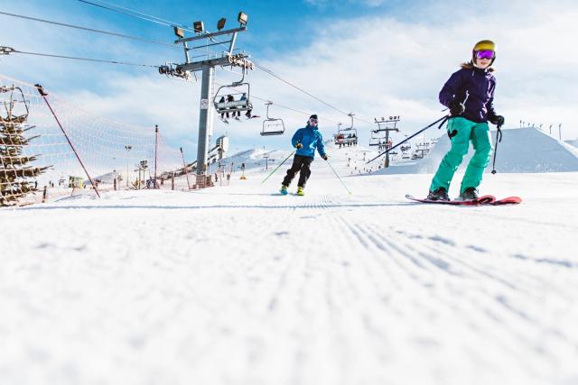 Two skiers heading down the hill, with the chairlift in the background, at WinSport.