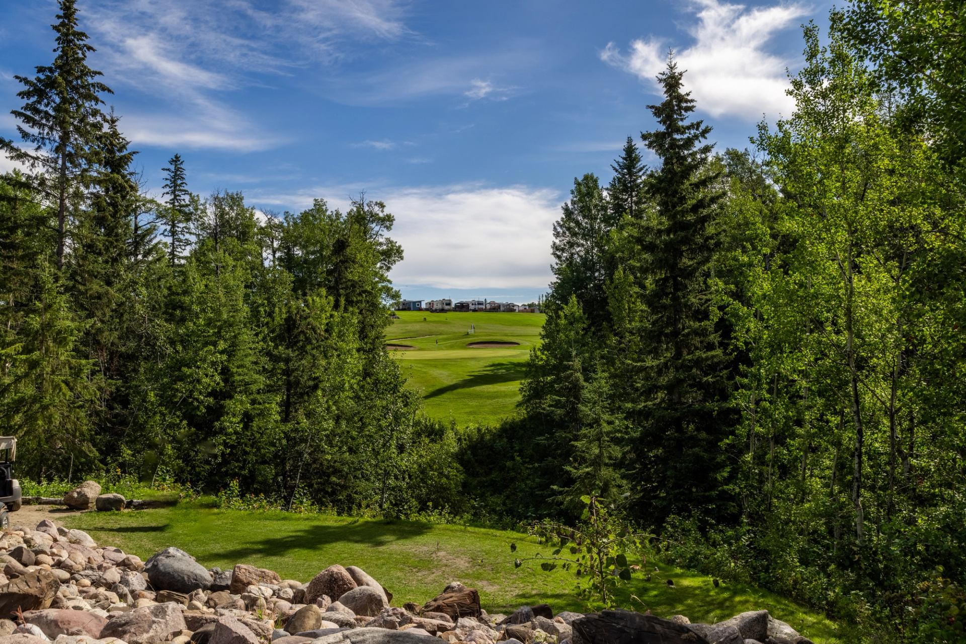Golf course framed by dense trees, with rocks in the foreground.