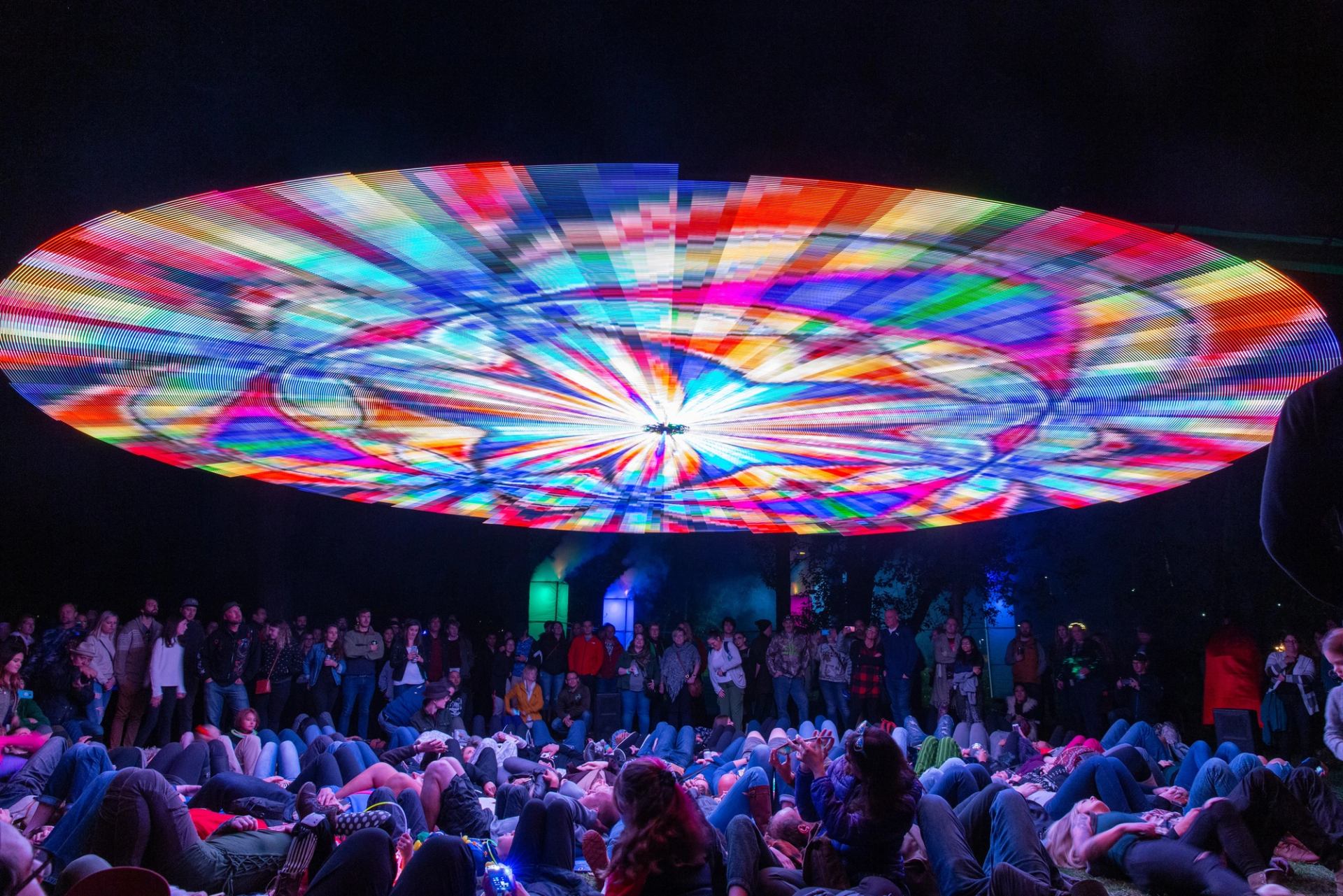 A colourful circle illuminates the ceiling of a room filled with people.