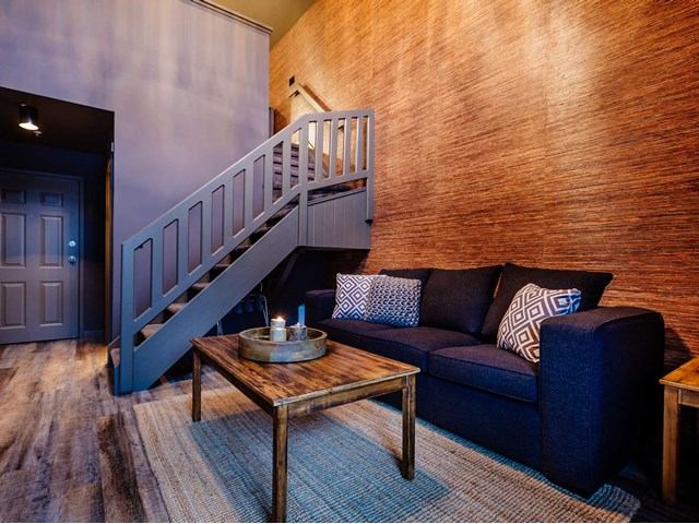 Living room with staircase, dark sofa, patterned pillows and wooden coffee table.