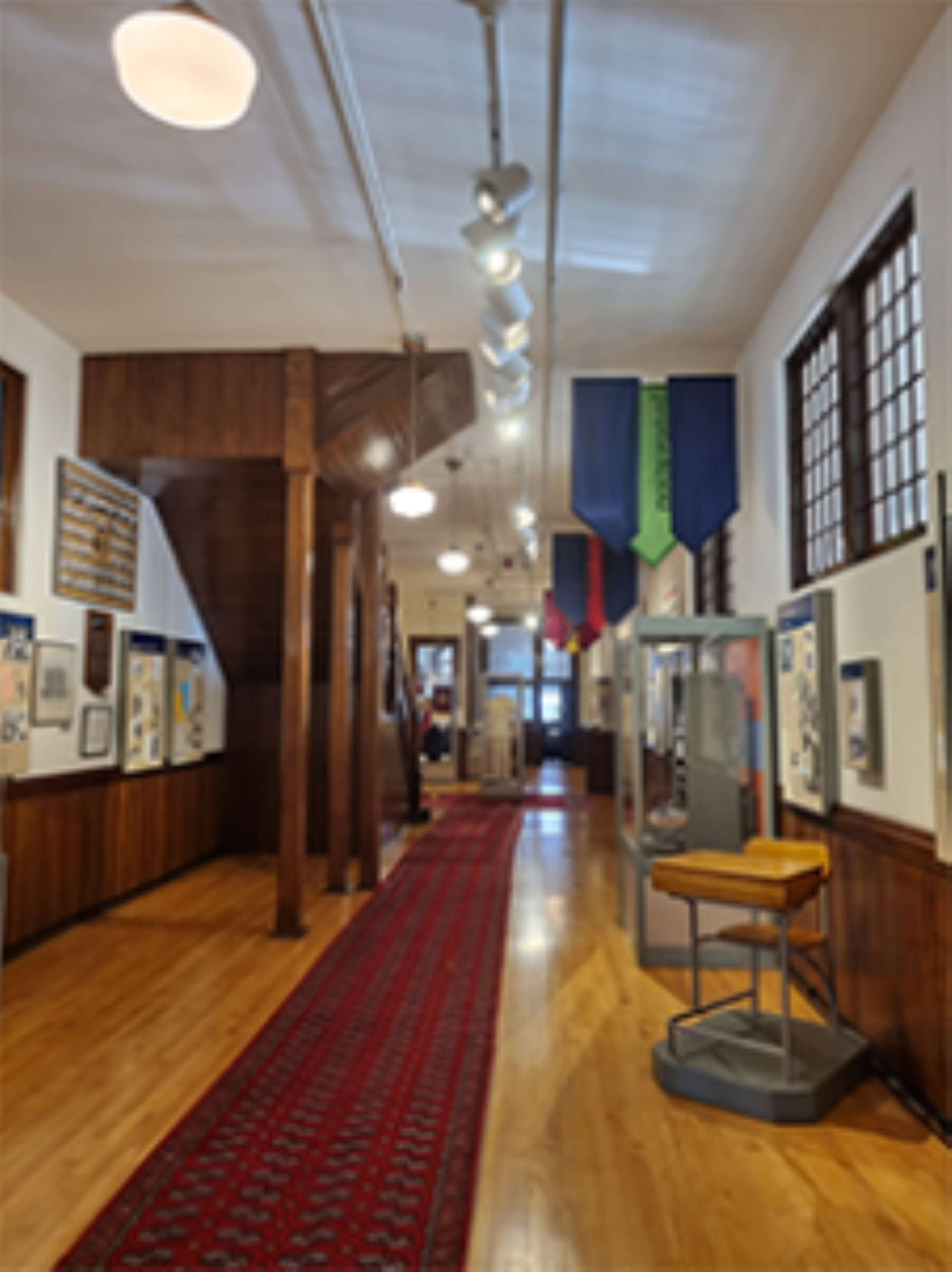 Museum hallway with red carpet, display cases, hanging banners and framed exhibits on walls.