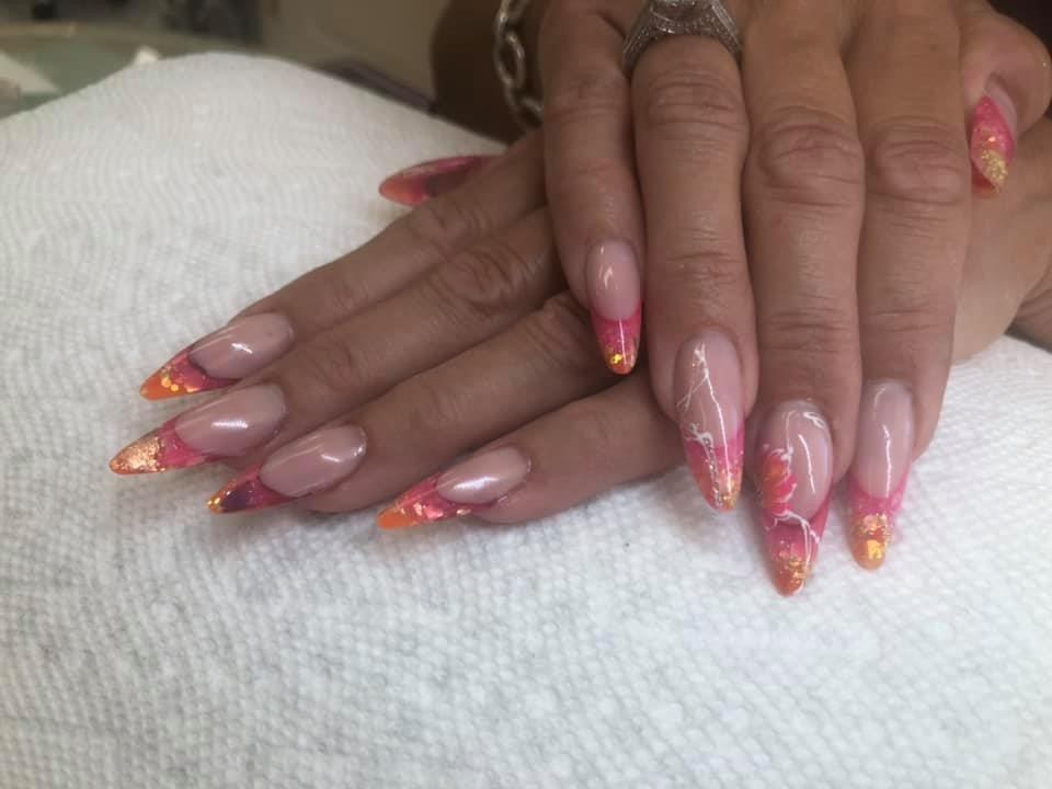 Hands with long pink-and-orange nail art resting on a white towel.