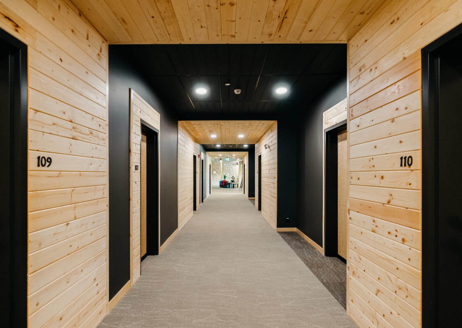 Wood-panelled hallway with numbered doors and recessed ceiling lights leading to lounge area.