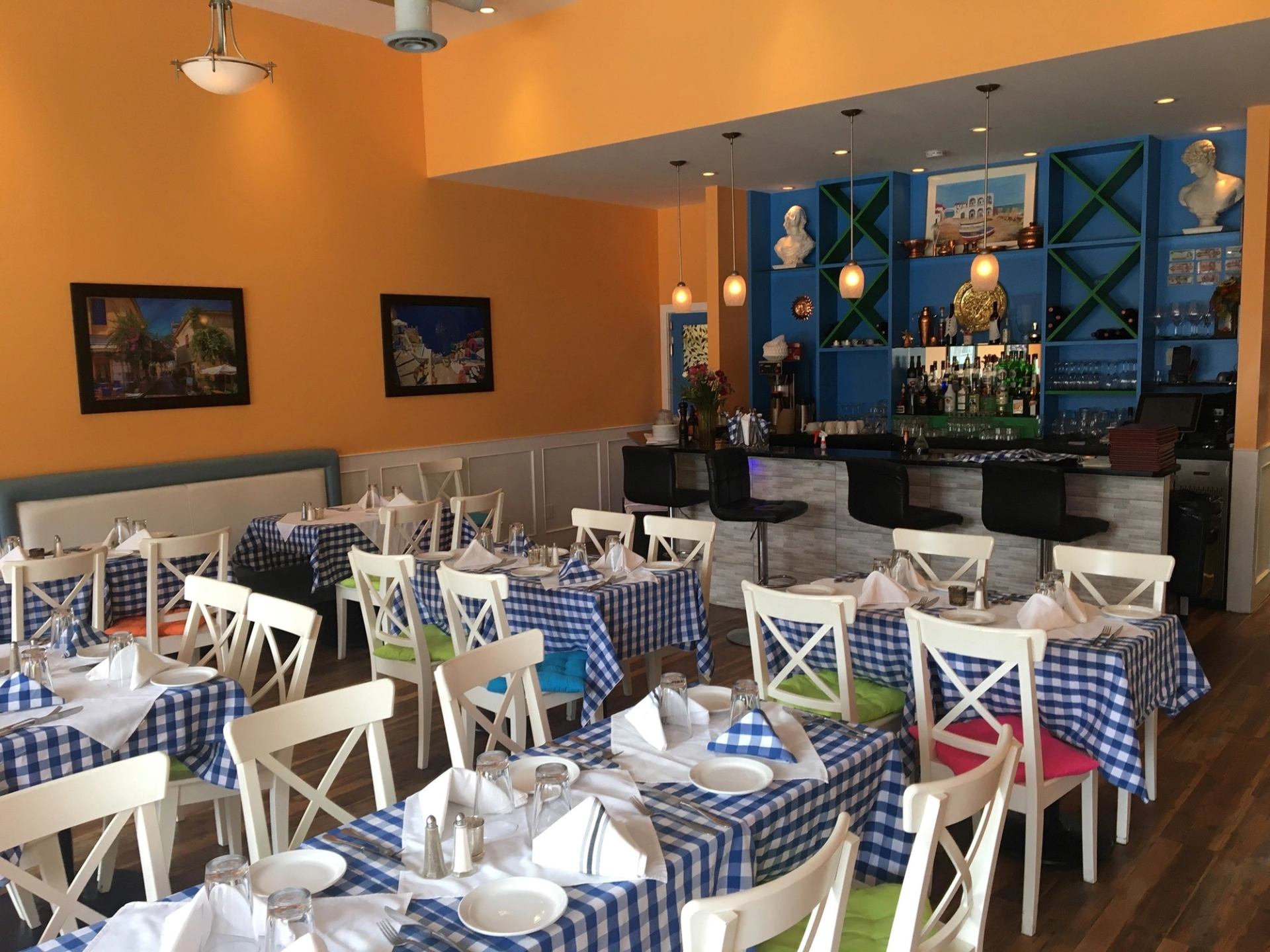 Colorful Greek taverna with checkered tables, vibrant chairs, and cozy bar area.