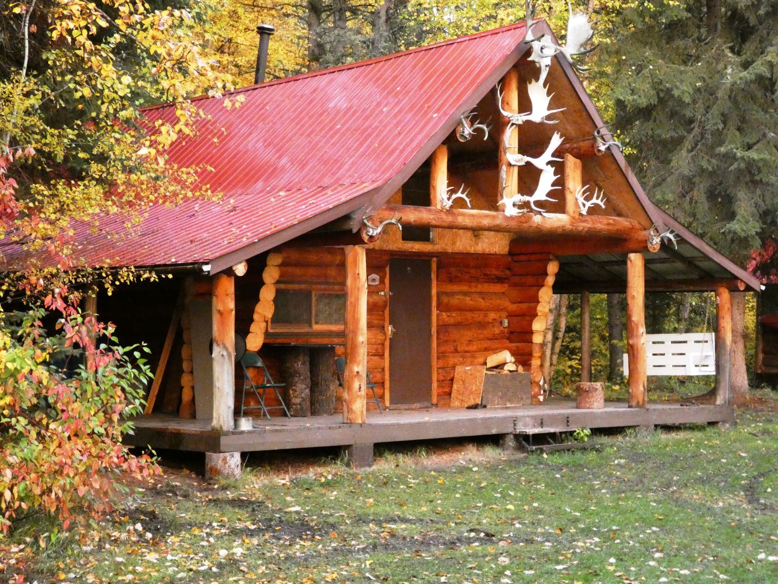 A cabin with a red roof and antler accents, framed by trees with autumn colors.