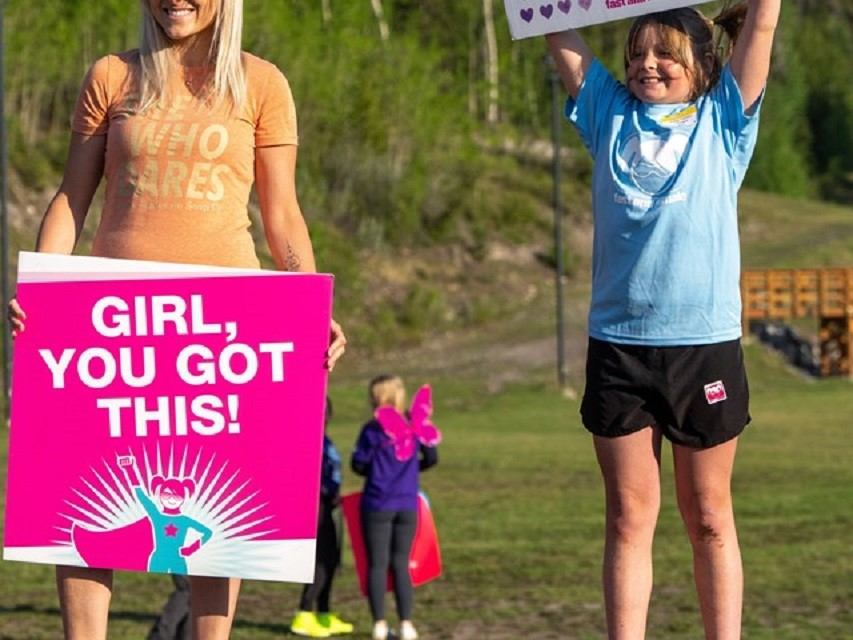 Runners hold signs on a grassy trail during a women’s soap run event.