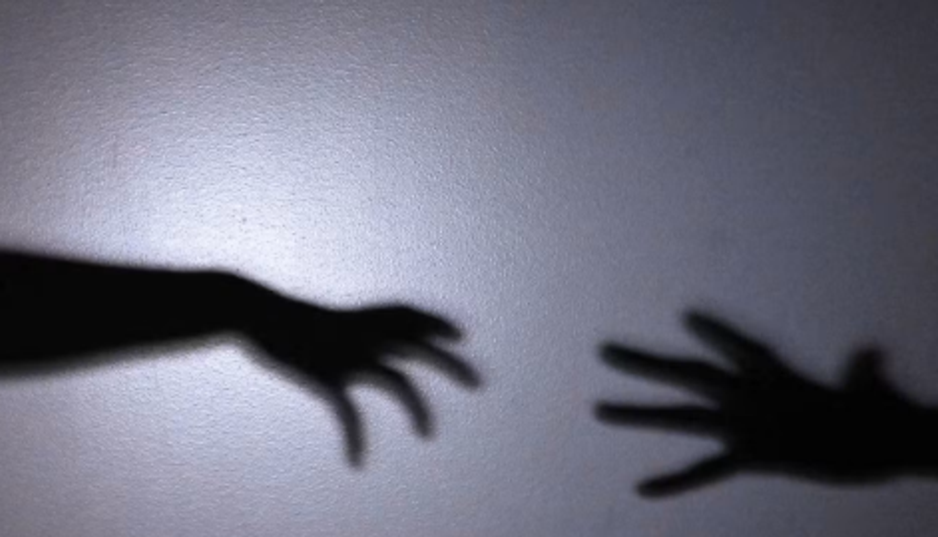 Shadows of two outstretched hands reach toward each other on a grey wall.