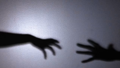Shadows of two outstretched hands reach toward each other on a grey wall.