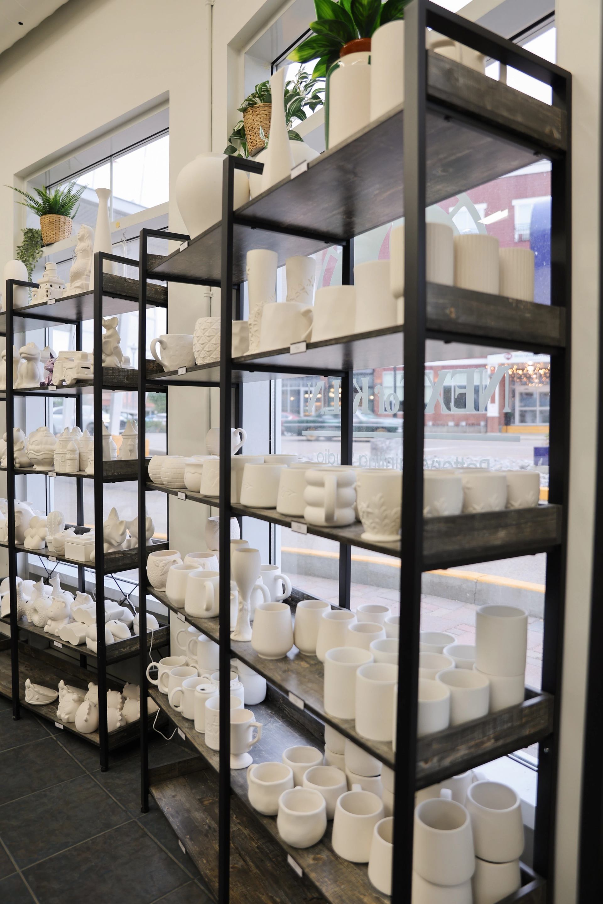 Shelving units display unpainted ceramic mugs, vases and figurines beside large windows.