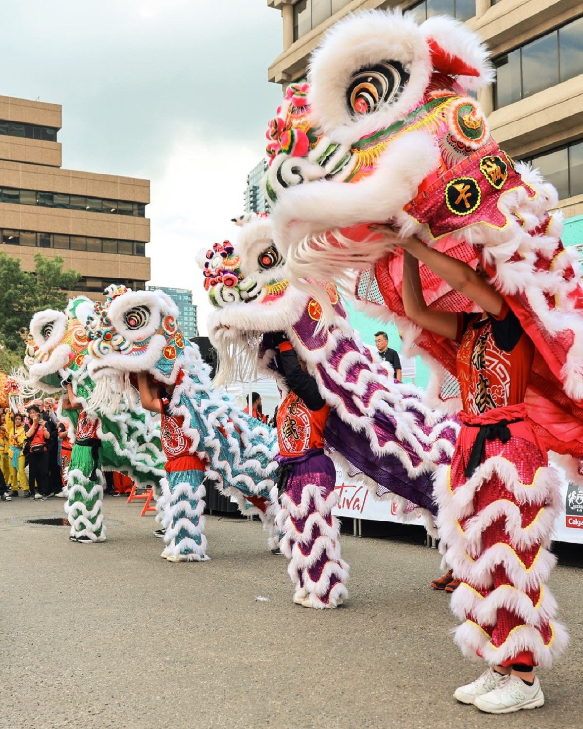 Four lion dancers performing in colorful costumes on city street.