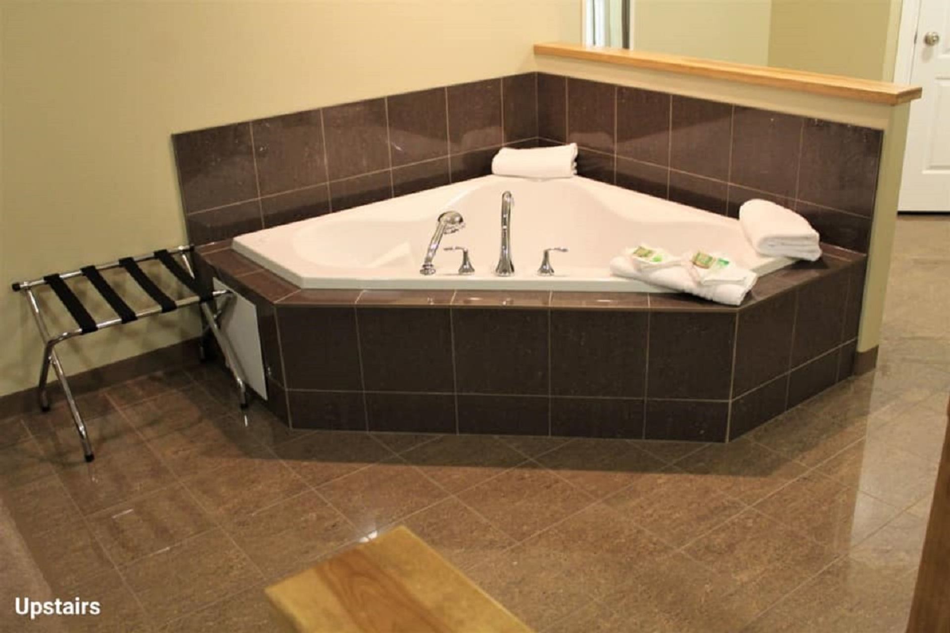Large jetted bathtub with tiled surround, folded towels, and bath amenities in a hotel suite.