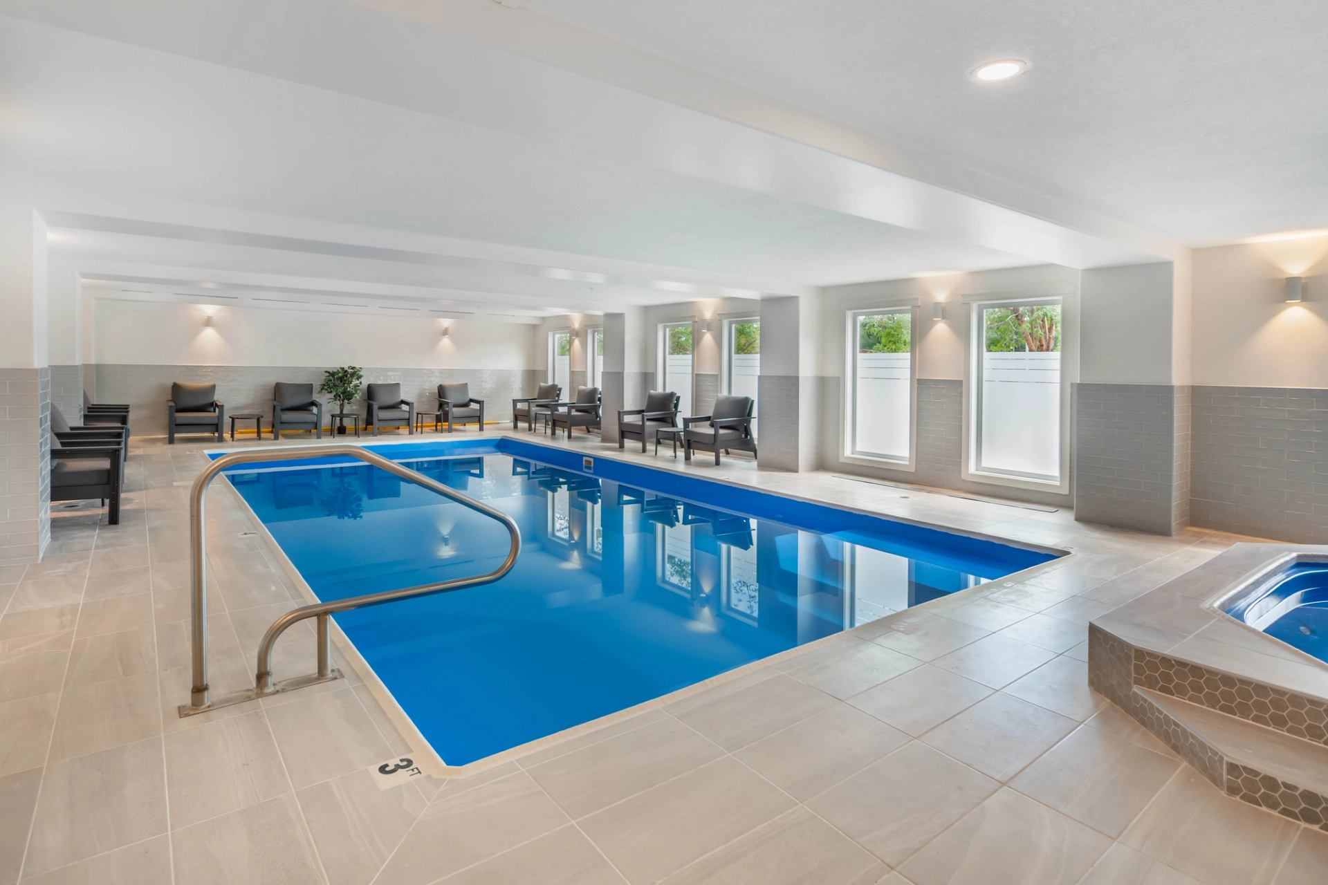 Indoor swimming pool area with bright lighting, lounge chairs, and a connected hot tub at Velora Hinton.