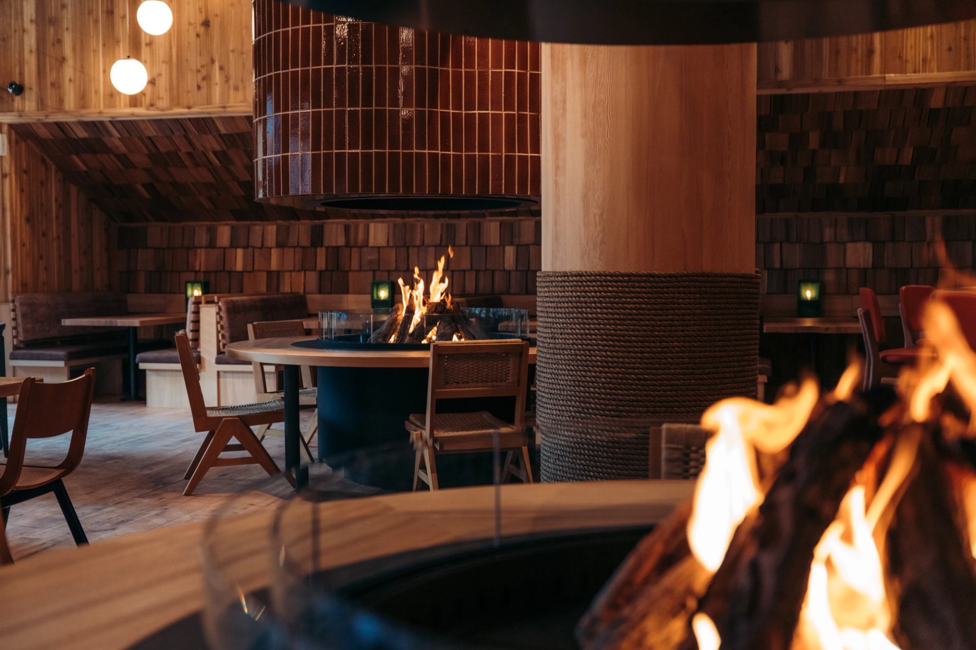 Wood‑lined restaurant interior with central fire and seating.