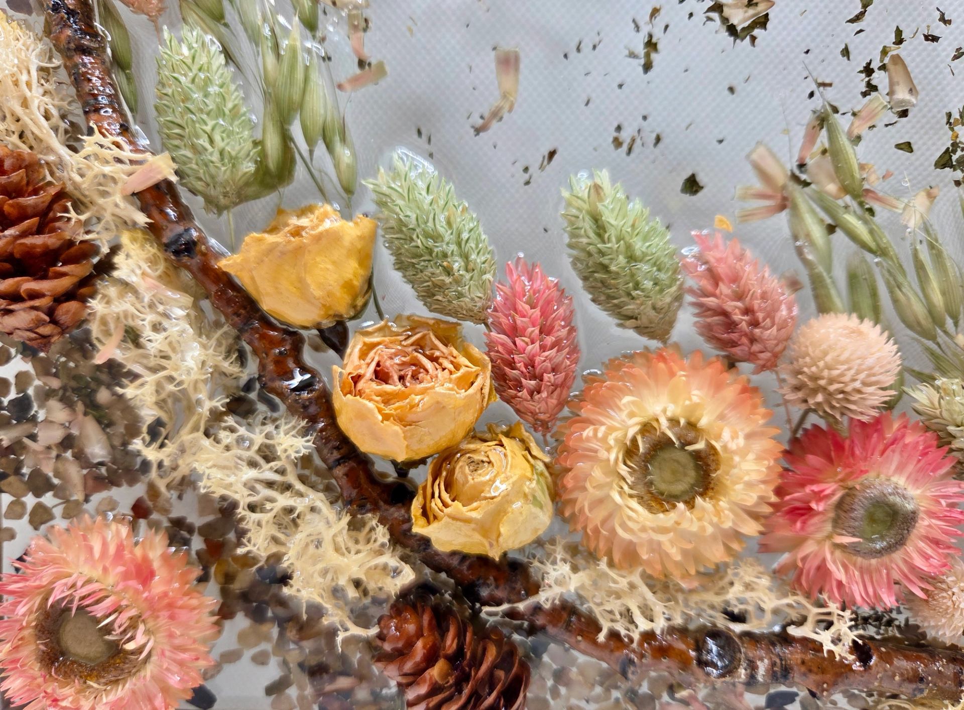 Pressed dried flowers, grasses and pinecones arranged on a curved branch in resin.