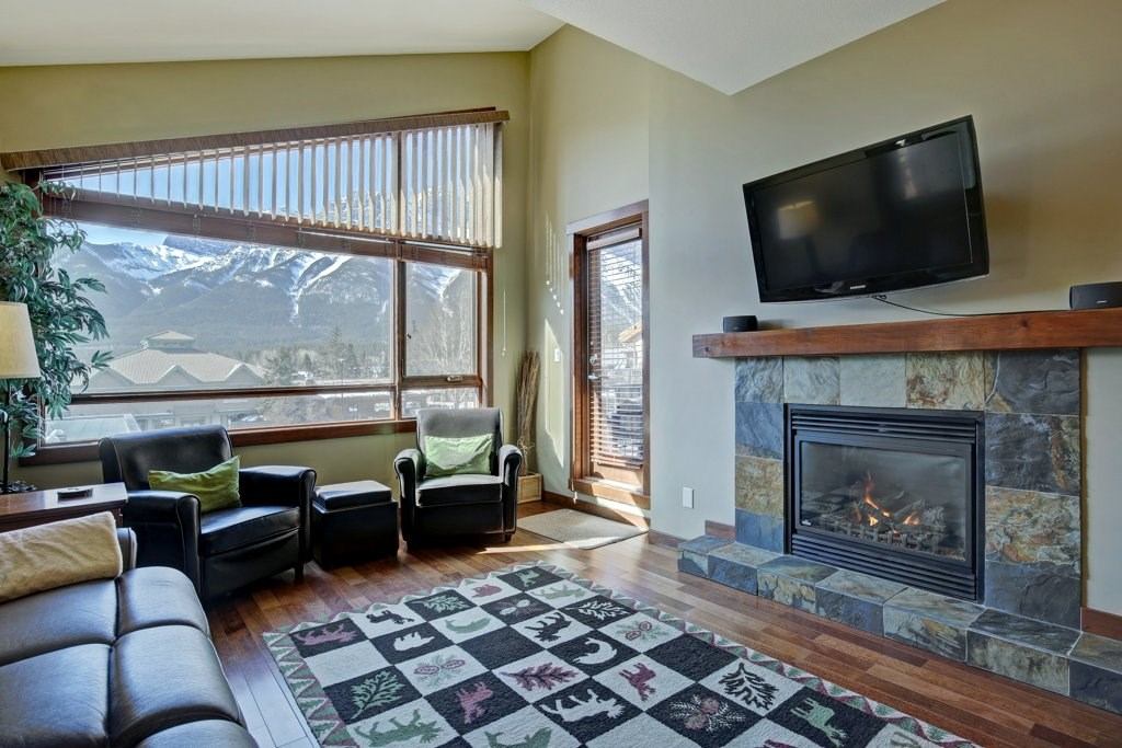 Living room with stone fireplace, wall-mounted TV, and large window showcasing mountain views.