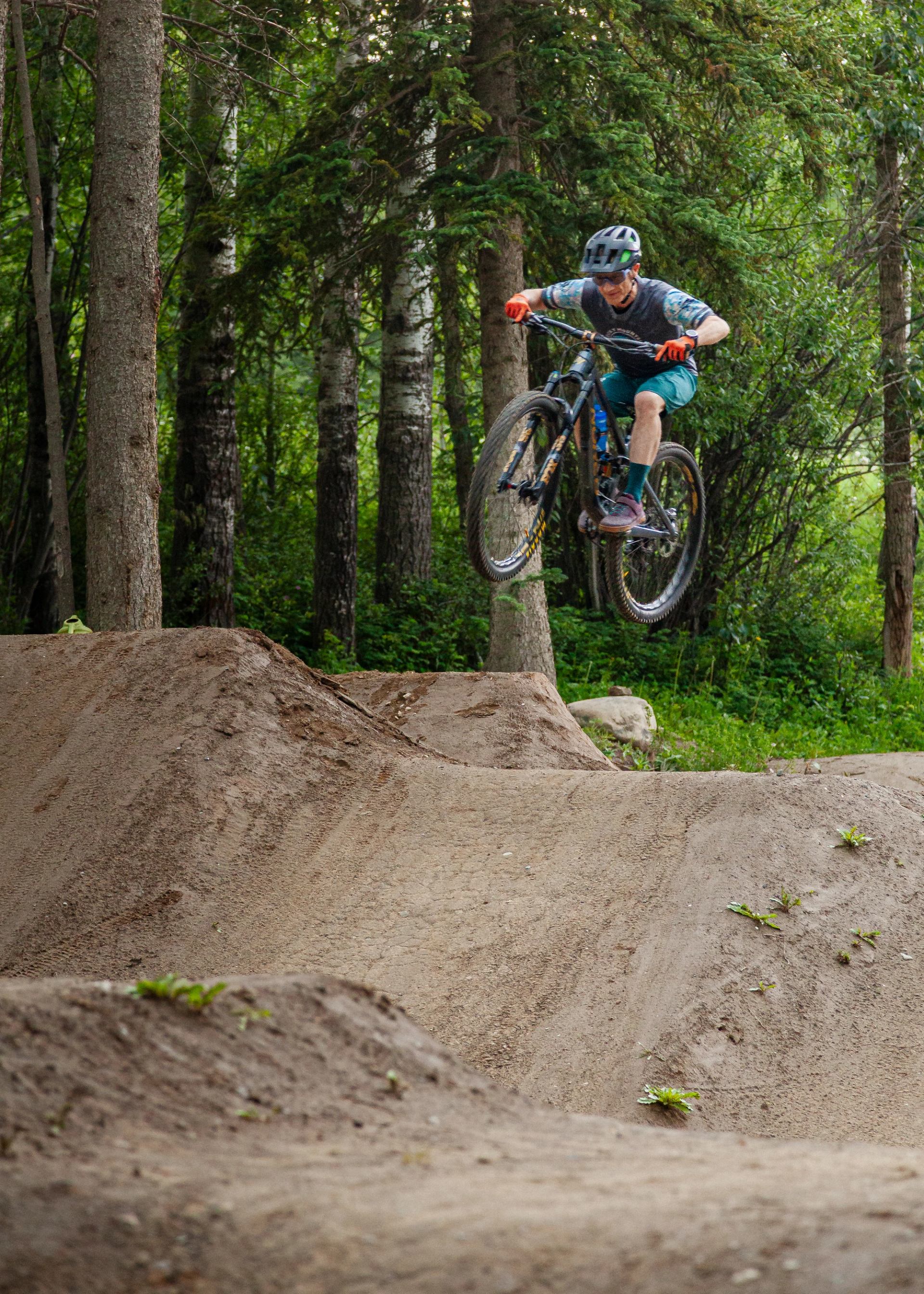 A mountain biker jumping over a dirt feature on a forest trail.