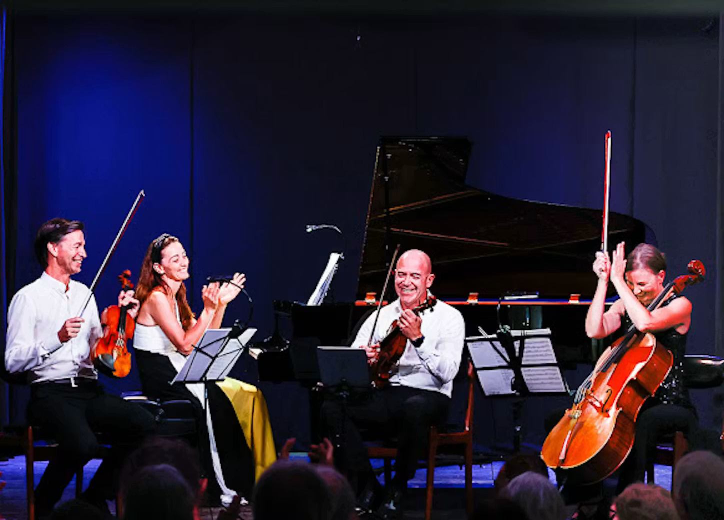 String quartet musicians on stage with violins, cello and grand piano, acknowledging audience.