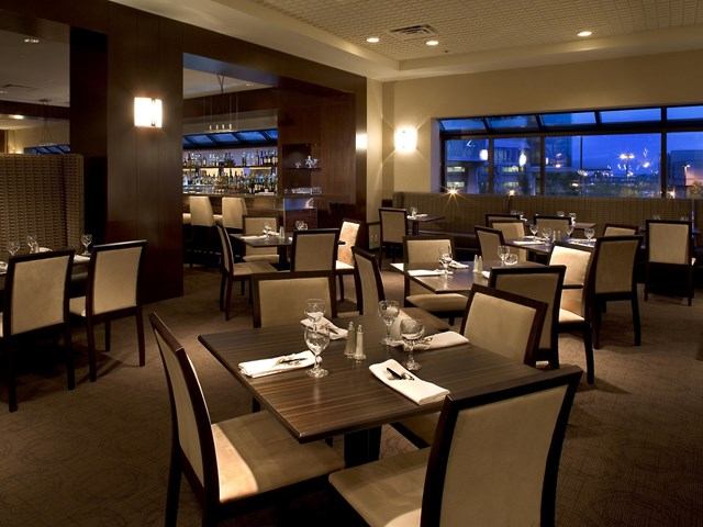 Elegant restaurant with city views, warm lighting, and neatly set tables at Delta Calgary Airport.