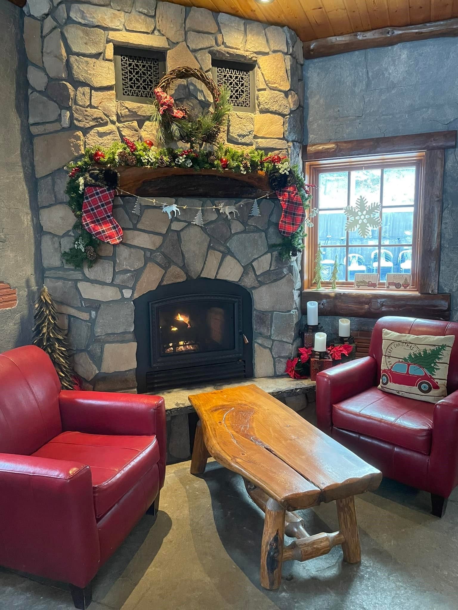 Stone fireplace with holiday décor, red chairs, and a wooden table in a cozy café corner.