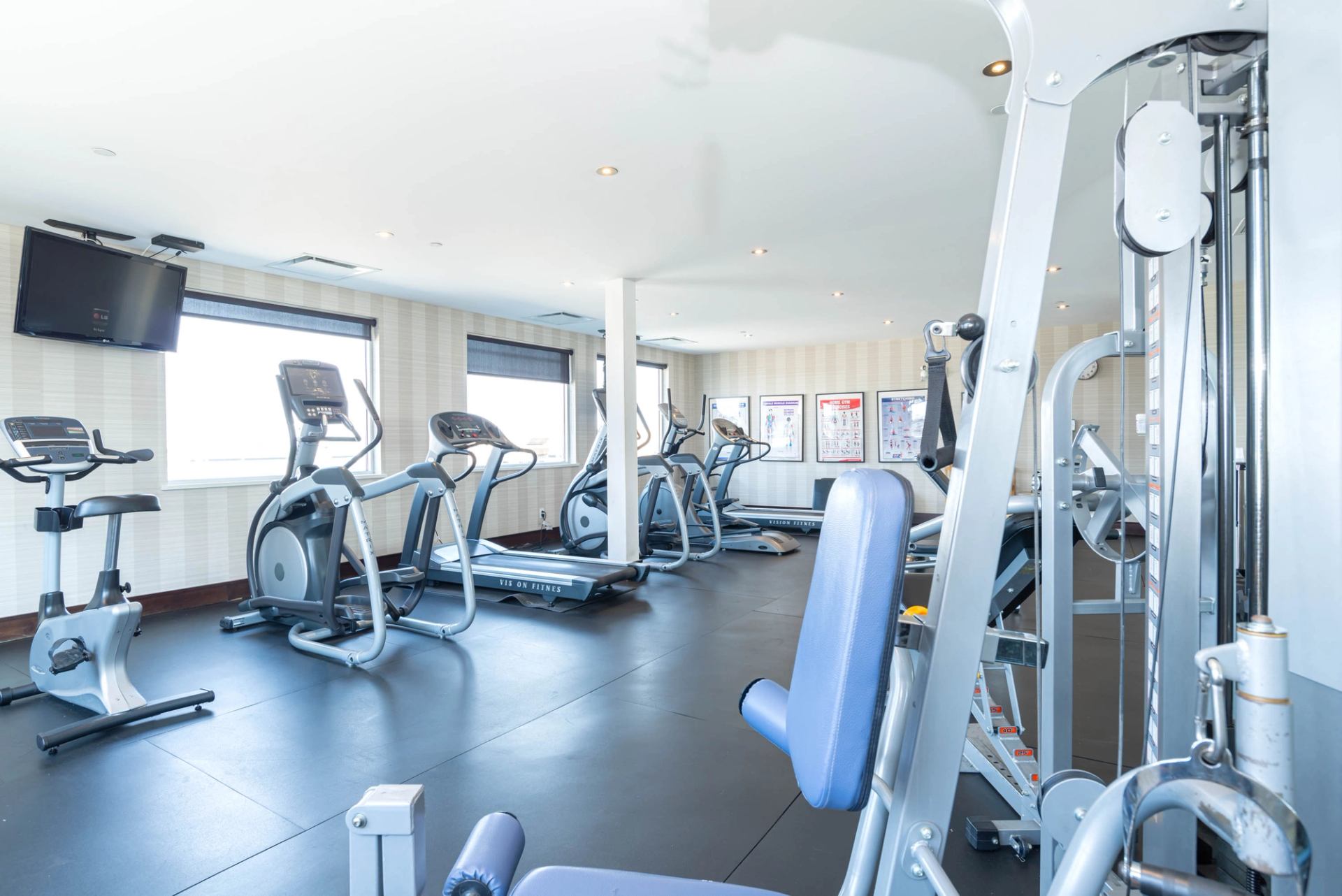 Hotel fitness room with cardio machines, weight equipment, and large windows.