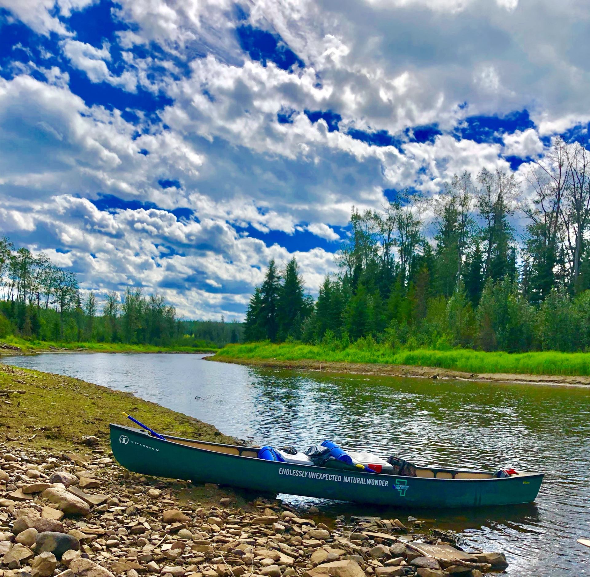 Canoe with gear on rocky riverbank under partly cloudy sky.