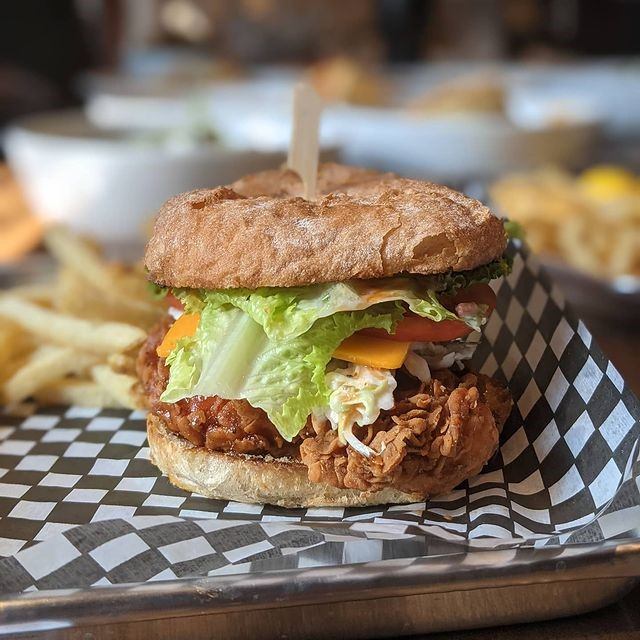 Fried chicken sandwich with lettuce, tomato, and cheese on a toasted bun.