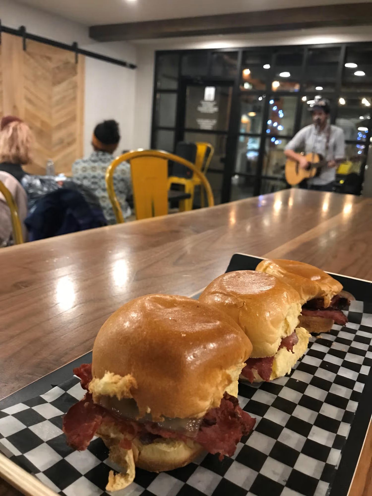 Mini meat sandwiches on a tray in café with musician playing guitar in background.