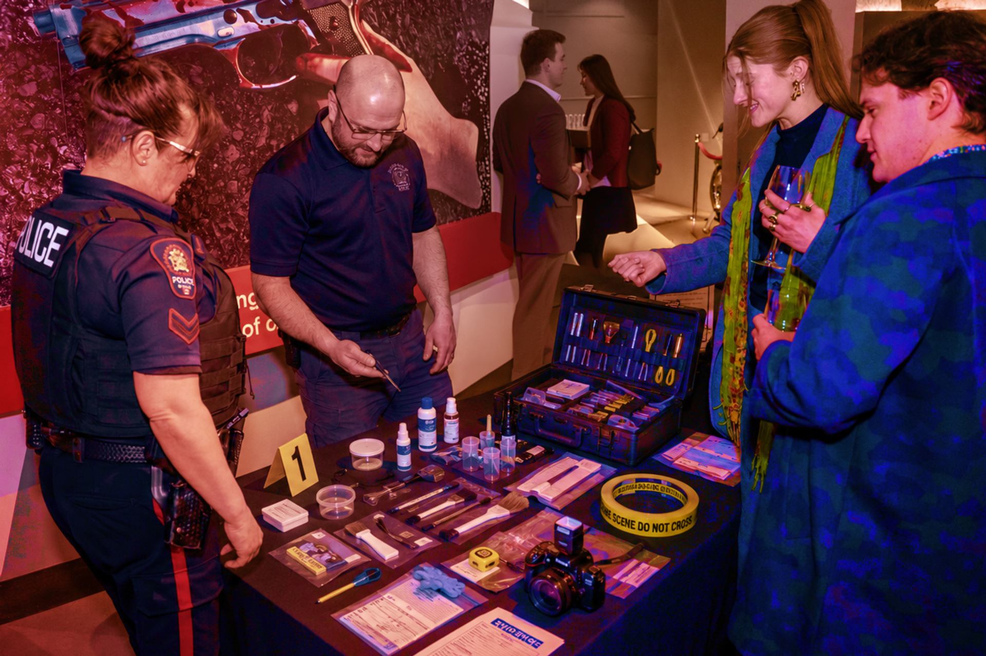 Police officer and civilians examine crime scene investigation tools displayed on an indoor table.
