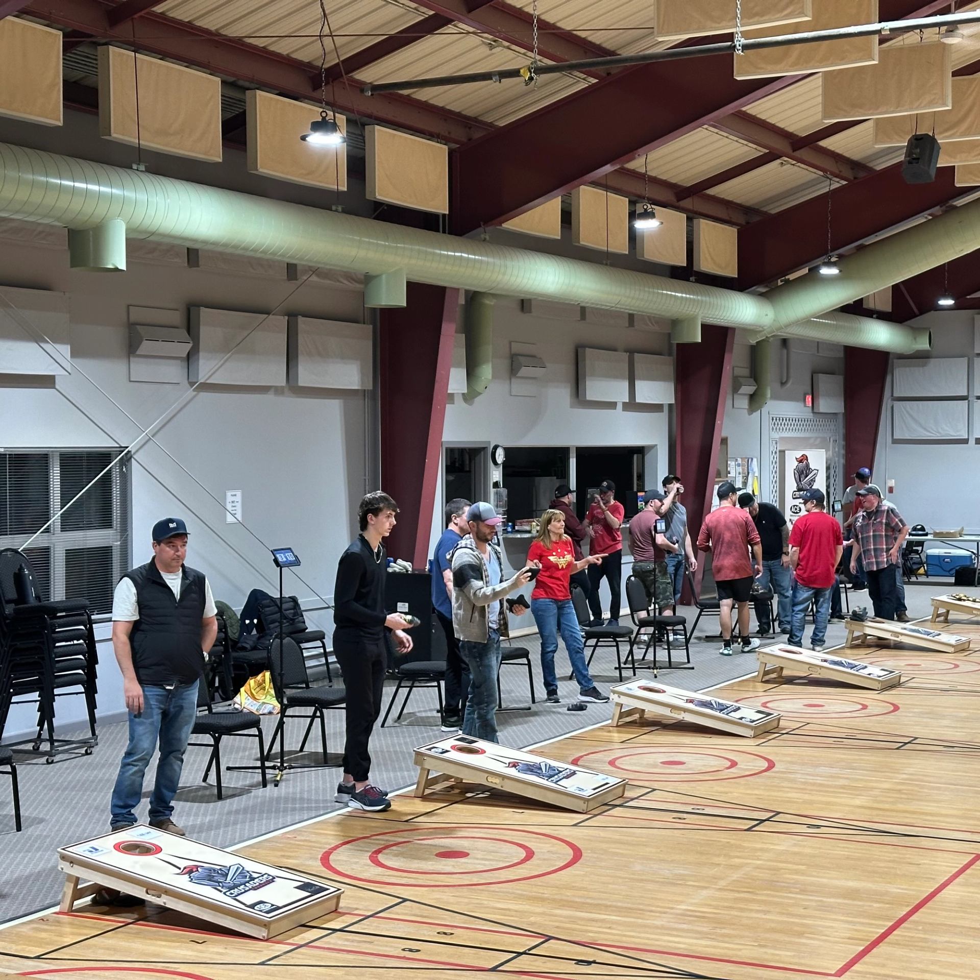 Row of players throwing bags across several cornhole boards indoors