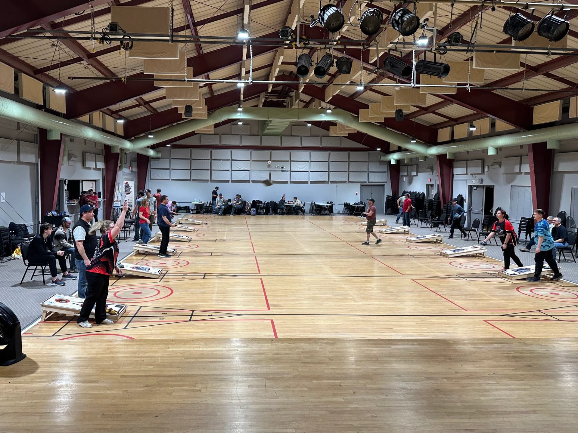 Large indoor hall with multiple cornhole lanes and players competing