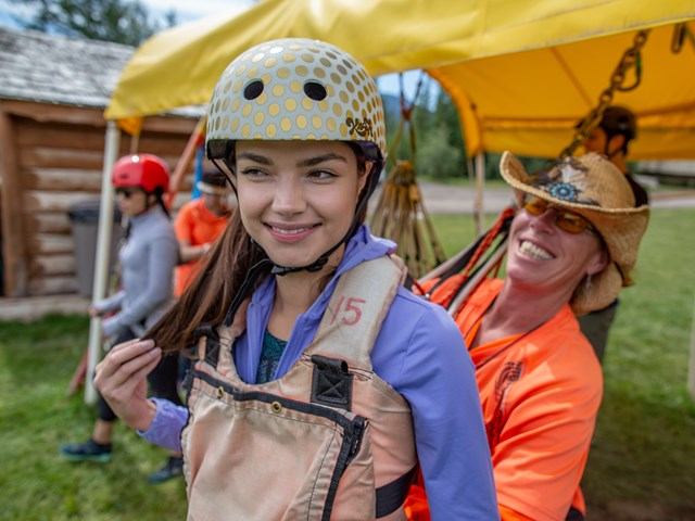 A woman in harness and helmet gets prepare for ziplining with help from support staff.