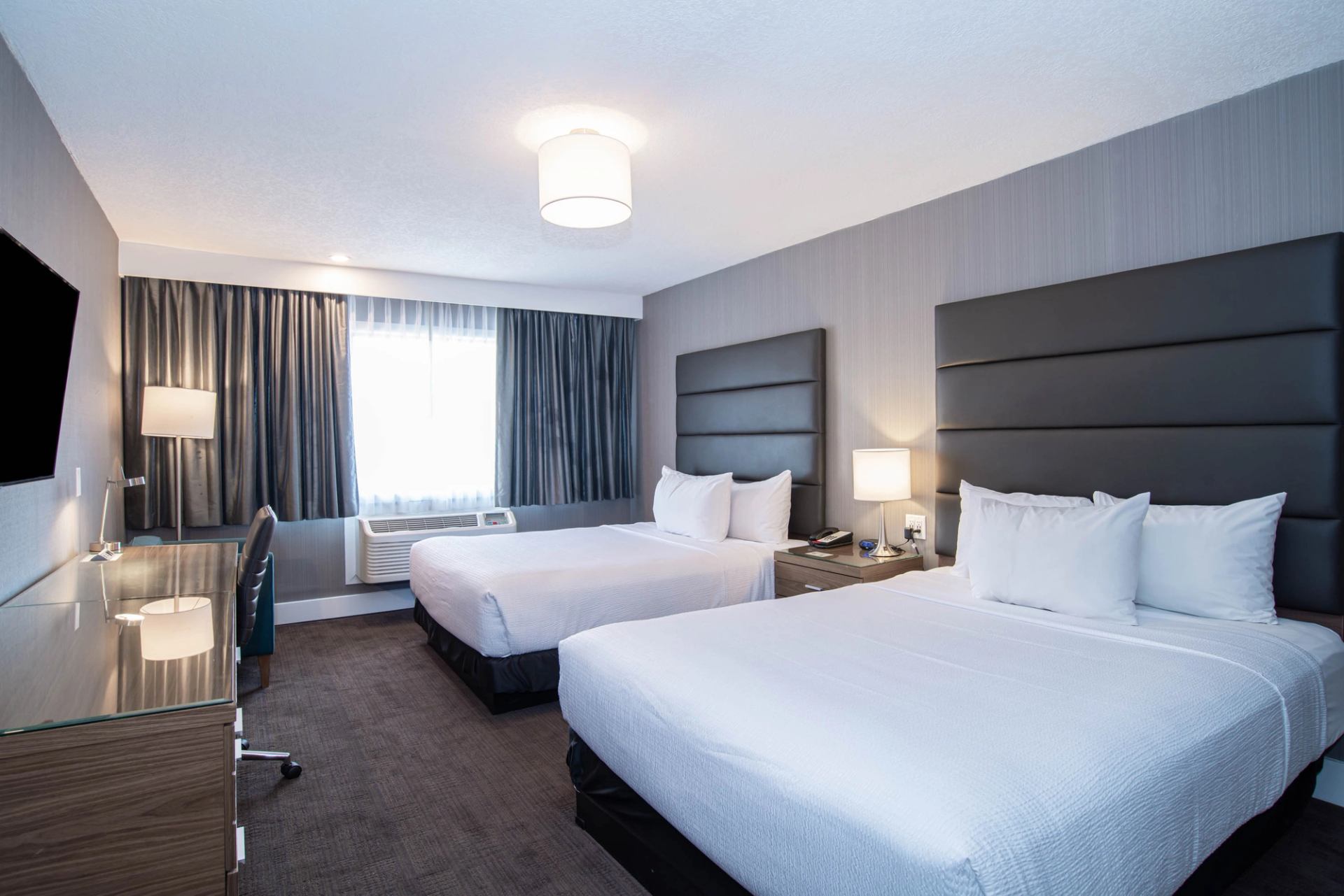 Hotel room with two double beds, desk, chair, window, and bedside lamps