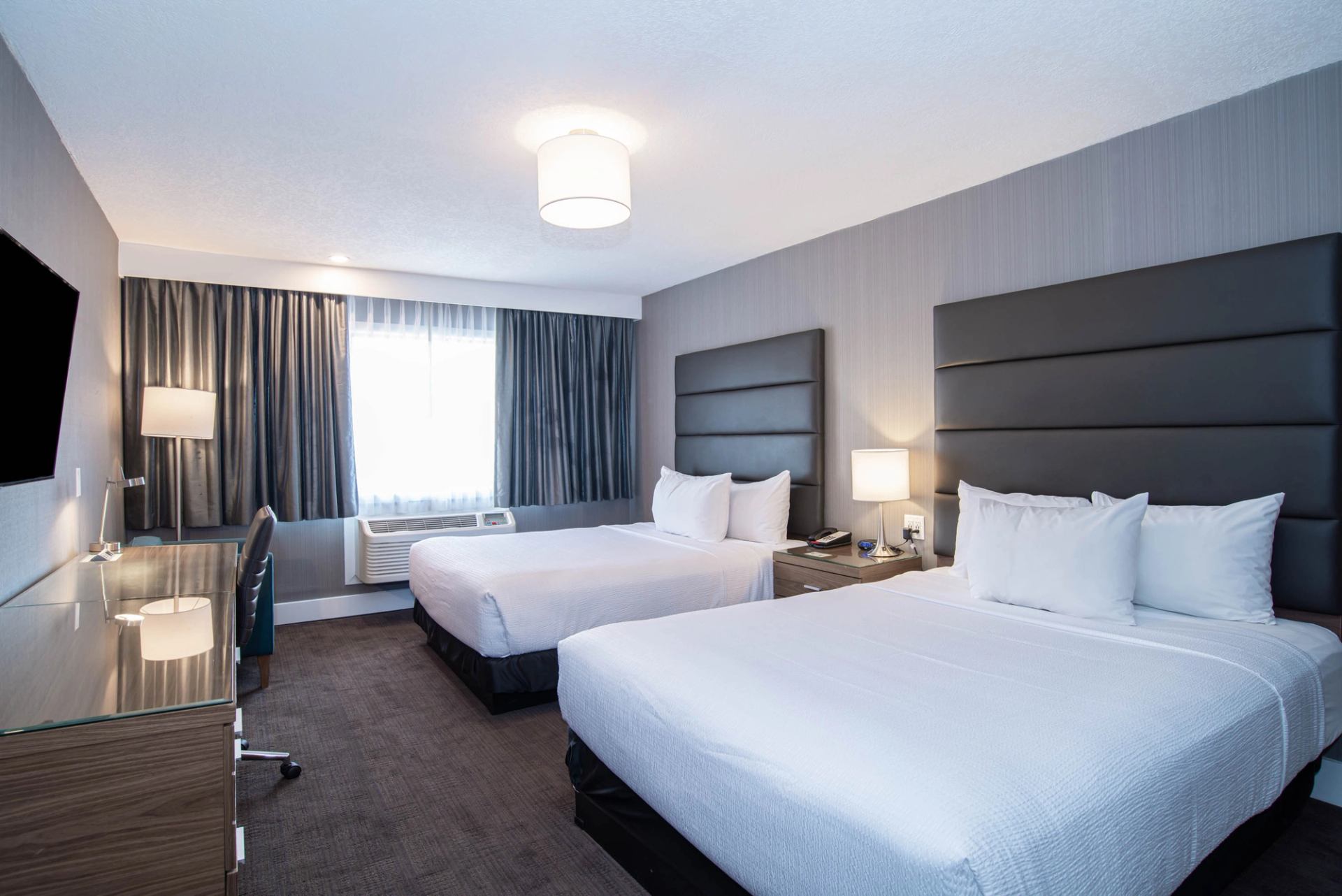 Hotel room with two double beds, desk, chair, window, and bedside lamps